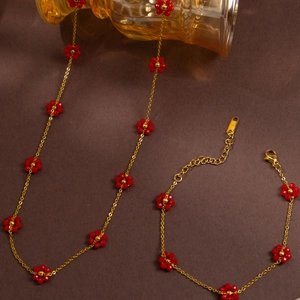 Detailed flat lay of golden stainless steel jewelry set with red beaded flower charms