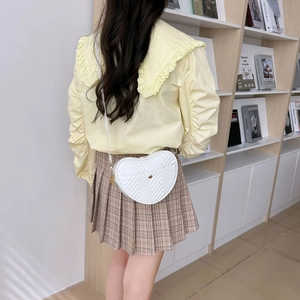 Stylish white heart-shaped quilted crossbody bag with gold hardware worn by a model