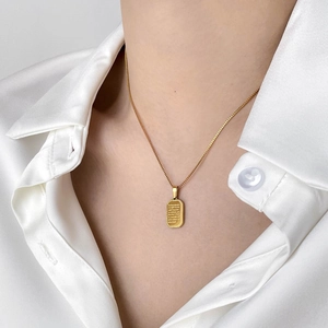 Macro shot of gold rectangle pendant with engraved text and detailed wheat border