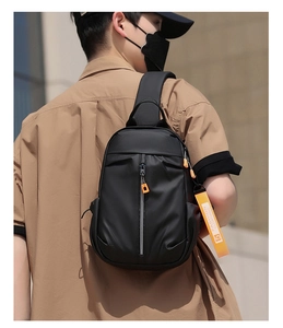 Rear view of trendy black crossbody sling bag with orange strap on male model