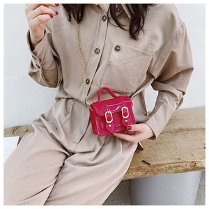 Close-up of pink mini jelly bag with gold chain strap worn by model against a wood background