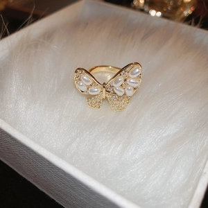 Macro shot of gold butterfly ring with inlaid pearls and crystals on plush surface
