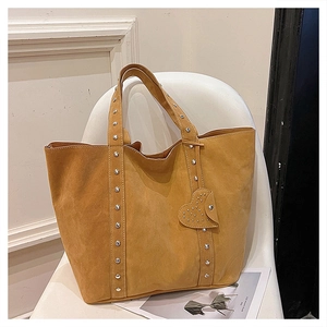 Detail of brown suede tote bag featuring metallic rivets and a heart shaped charm
