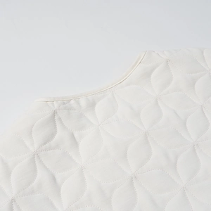 Detailed macro view of cream quilted jacket featuring petal patterns and round neckline