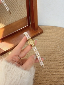 Detailed close-up of a vintage oval gold watch featuring a double-row pearl strap