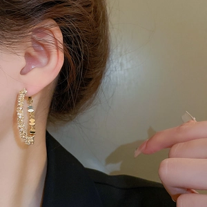 Gros plan d'une boucle d'oreille en C dorée sertie de zircons portée par un modèle