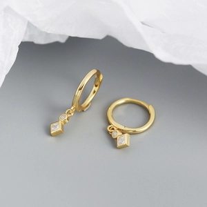 Detail of gold hoop earrings with square and round zircon charms on white paper