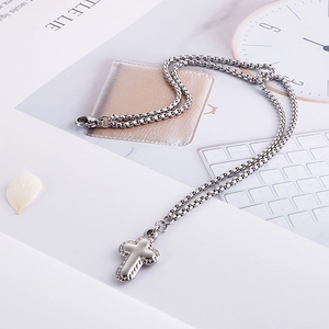 Vista macro del ciondolo a croce argento con texture e catena a maglia veneziana