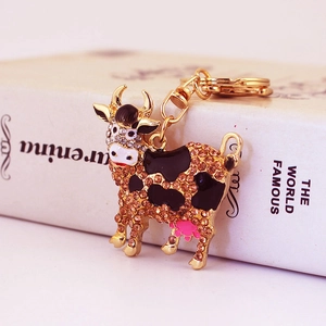 Cute cow keychain with colorful crystals and gold-plated finish on minimalist book background