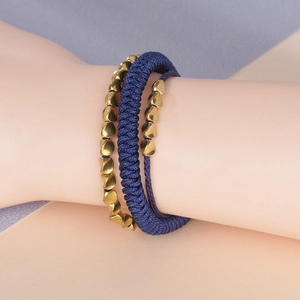 Detail showing hand-woven blue cord bracelet paired with gold heart-shaped bead strand