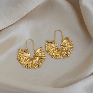 Vue détaillée de boucles d'oreilles dorées en forme d'éventail plissé sur tissu en soie