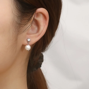 Detailed close-up of a silver C-shaped earring with white pearl and sparkling zircon