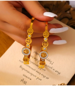 Close-up of gold Tree of Life earrings with zircon stones held against a vintage background