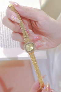 Close-up of a women's gold square watch with a diamond-set bezel and mesh metal strap