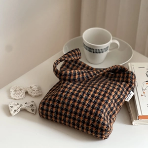 Detail of checkered knit handbag with woven label on a minimalist decorative tabletop