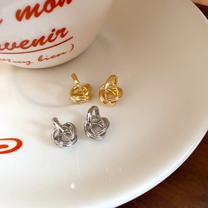 Detail view of gold and silver minimalist twisted knot earrings in a ceramic dish
