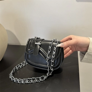 Minimalist black leather saddle bag with silver chain strap shown in a hand-held view