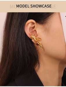 Close-up of golden ribbon-shaped earring with white rhinestone on female model ear