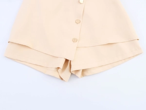 Detail view of light apricot skort with asymmetric hem and decorative gold buttons