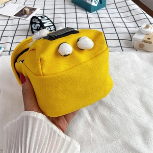 Detail of yellow canvas crossbody bag featuring white pom-poms and lettered strap