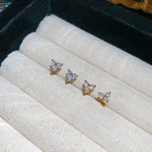 Macro shot of two floral stud earrings with tiny zircons displayed in a beige jewelry box