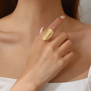 Macro shot of irregular golden oval metal ring with brushed matte finish on model's finger