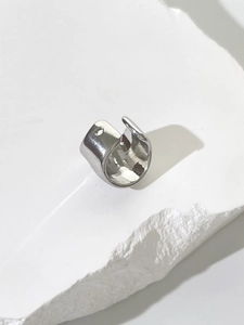 Macro shot of minimalist silver U-shaped ear cuff placed on white textured stone surface