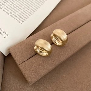 Detailed view of matte golden brushed metal hoop earrings on a textured display stand