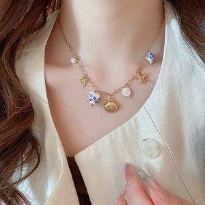 Dettaglio della collana dorata con cuore blu, conchiglia e ciondoli di perle sul collo