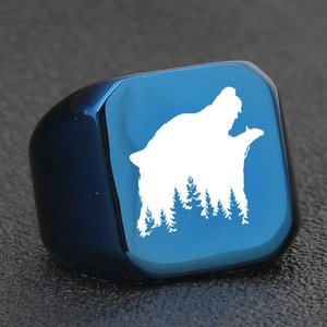 Macro shot of square dark blue ring face with white laser-engraved wolf and forest design