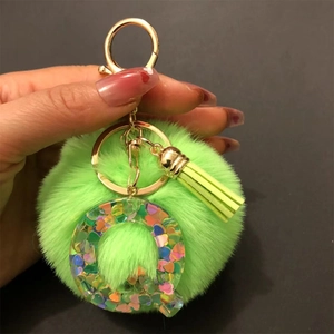 Detailed close-up of a bright green fluffy pompom keychain with a clear resin letter Q charm