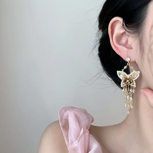 Gros plan de boucles d'oreilles papillon dorées avec cristaux roses et longs pompons