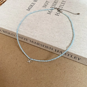 Detail of blue beaded necklace with a silver starfish pendant on a rustic wooden background