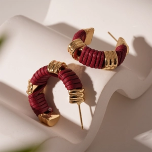 Détail macro de boucles d'oreilles C en similicuir rouge tressé avec des accents dorés