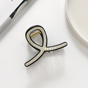Detail of a beige striped hair claw clip with black piping and gold-toned metal spring