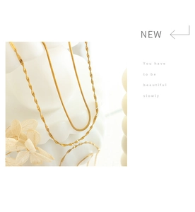 Detail of double-layered gold snake chain and twisted link necklace on a white pedestal