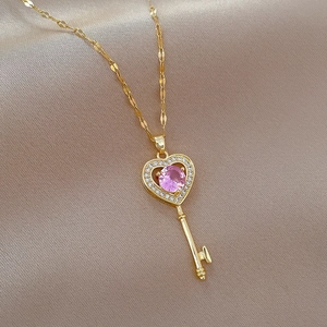Elegant gold heart key necklace with pink gemstone and crystals on beige silk