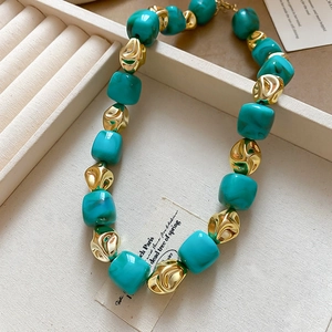 Macro detail of teal faux-stone beads and gold textured metal beads on a beige jewelry tray