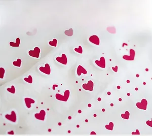 Macro detail of red heart nail art stickers featuring varied dots on white fabric