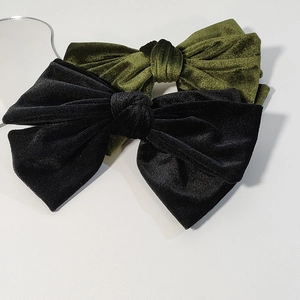 Close-up of elegant black and olive green velvet bow hair clips on white surface