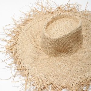 Detailed shot of wide-brim straw sun hat featuring decorative frayed edges and woven texture