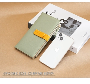 Long green leather wallet size comparison with a white iPhone on a beige desk