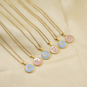 Détail de colliers dorés 18 carats avec pendentifs ronds en nacre colorée et lettres
