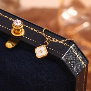 Close-up of a gold clover shell necklace displayed on a black velvet jewelry box