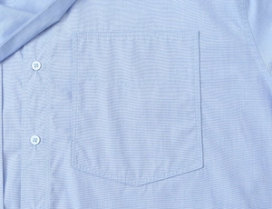 Macro view of light blue shirt fabric texture with white buttons and a single pocket