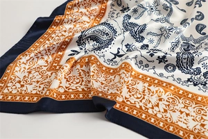 Close-up of paisley pattern silk scarf with geometric border in navy and orange
