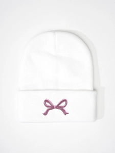 Detailed close-up of a white knit beanie featuring purple bow embroidery on the folded cuff