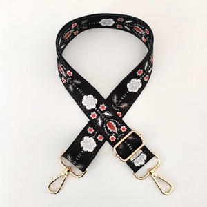 Detail of ethnic floral embroidery on black webbing bag strap with gold metal hardware