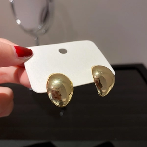 Detailed view of irregular golden pebble stud earrings held against a white card background
