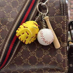 Detail of mini baseball glove, bat, and ball keychain hanging on a stylish brown handbag